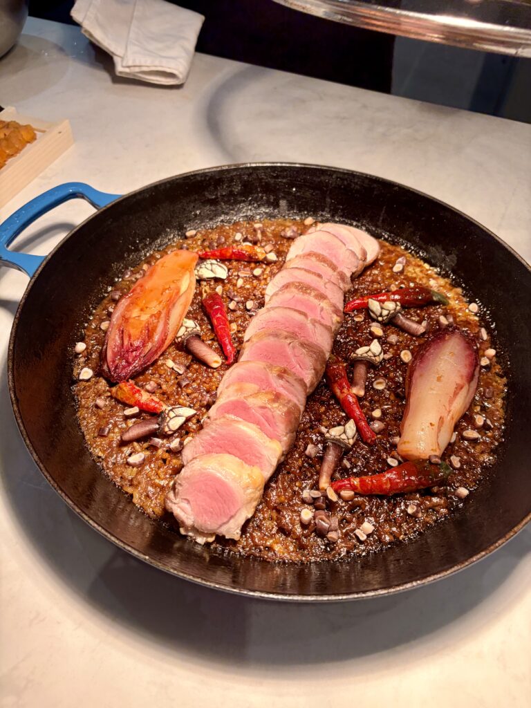 ปาเอญ่าในกระทะสีดำ มีหมูอิเบริโกหั่นเรียงตรงกลาง Goose Barnacle และ Red Endive วางรอบข้าว